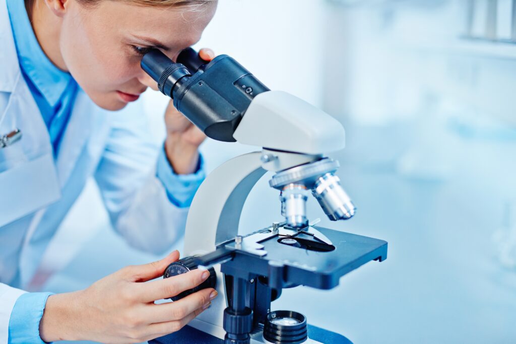 Young female chemist looking at cancer cells in a microscope